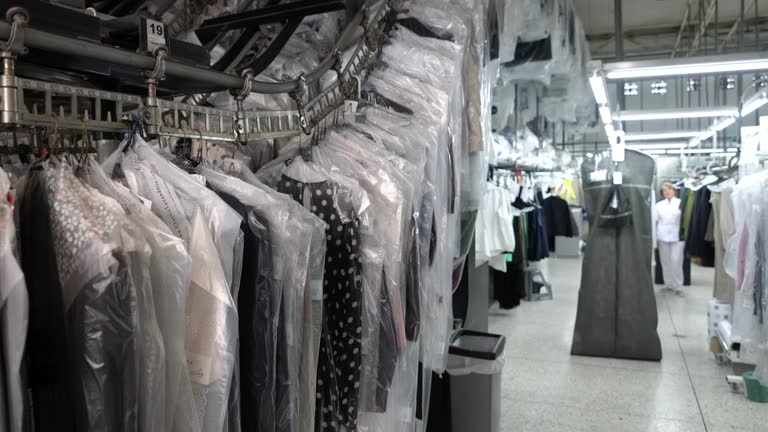 Clean garments on conveyor belt at an industrial dry cleaning service and woman operating at background